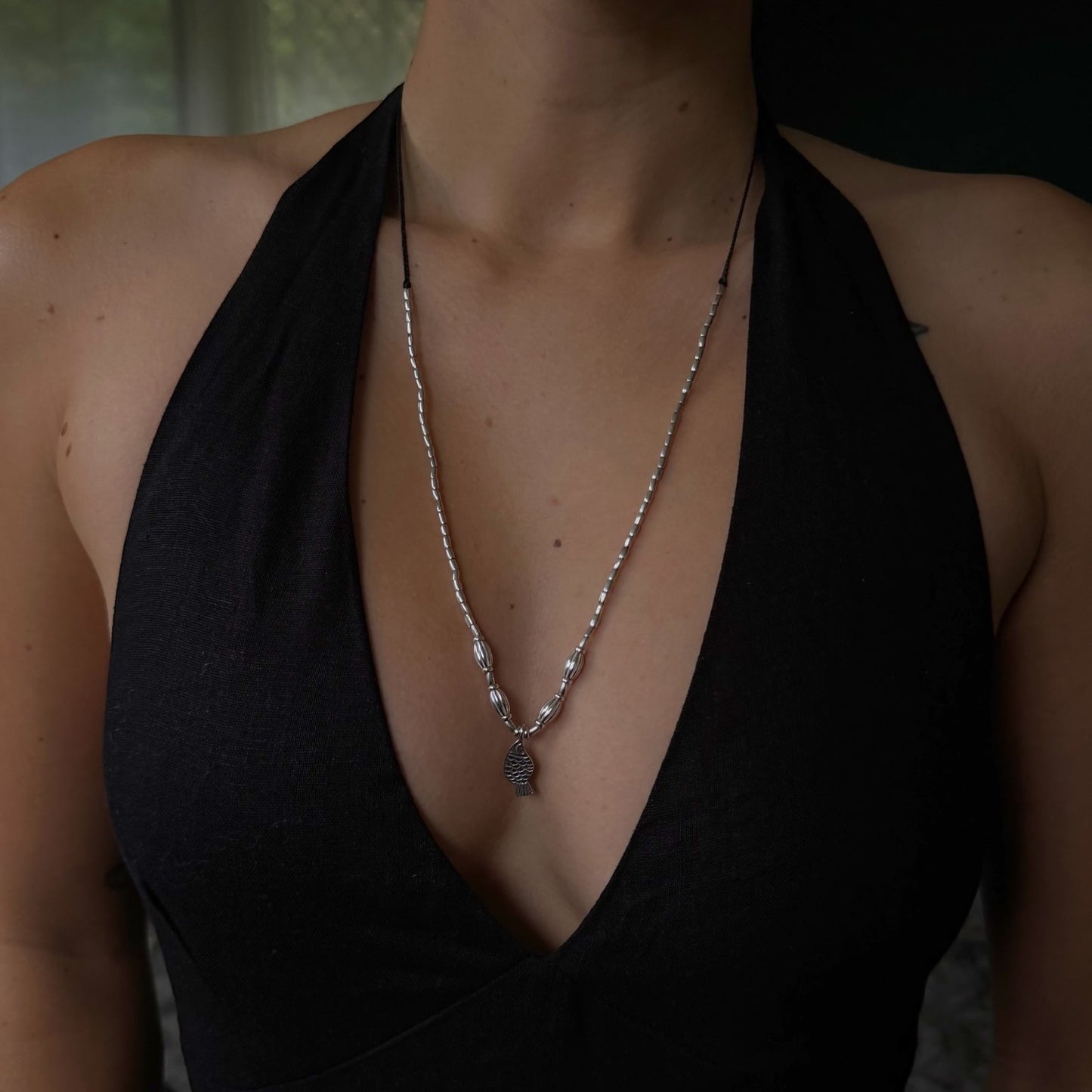 Person wearing a black halter top with a necklace featuring a tree pendant.