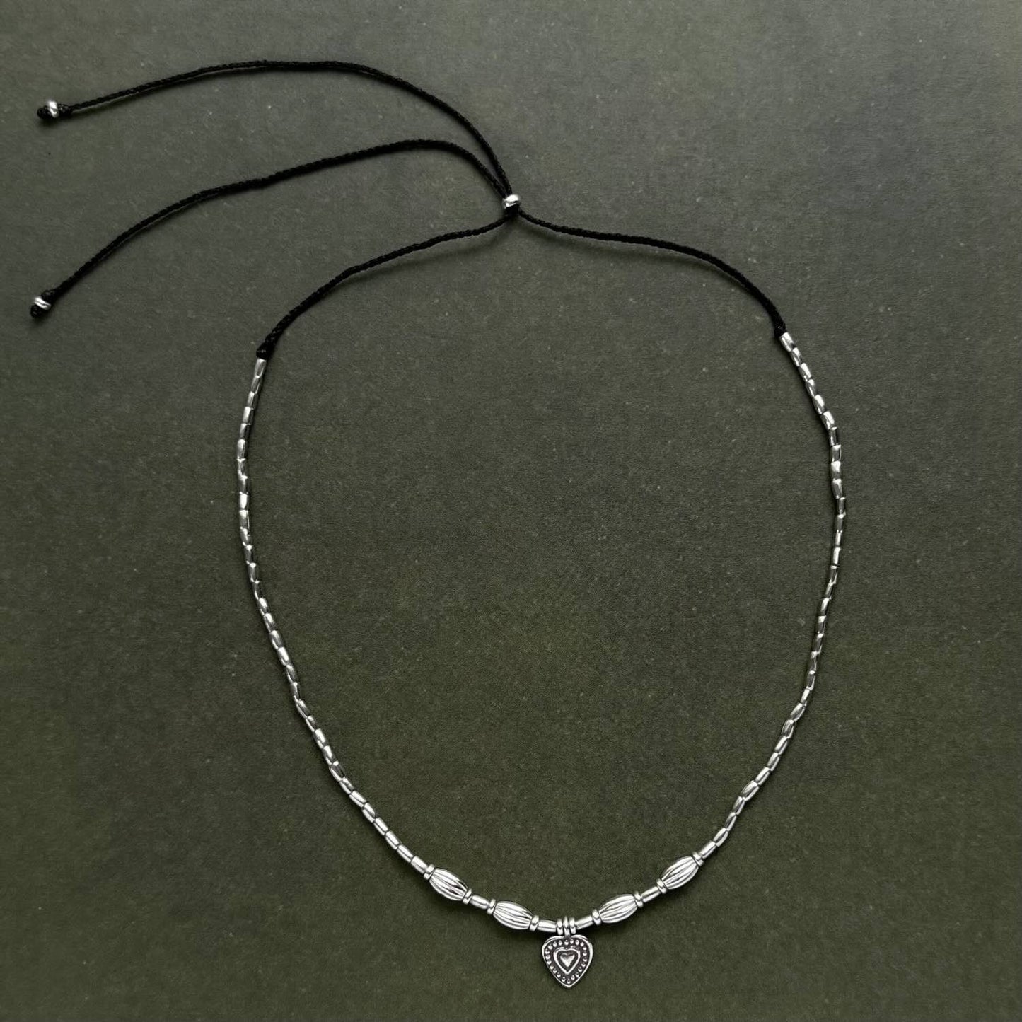 Silver beaded necklace with a heart charm on a dark green background