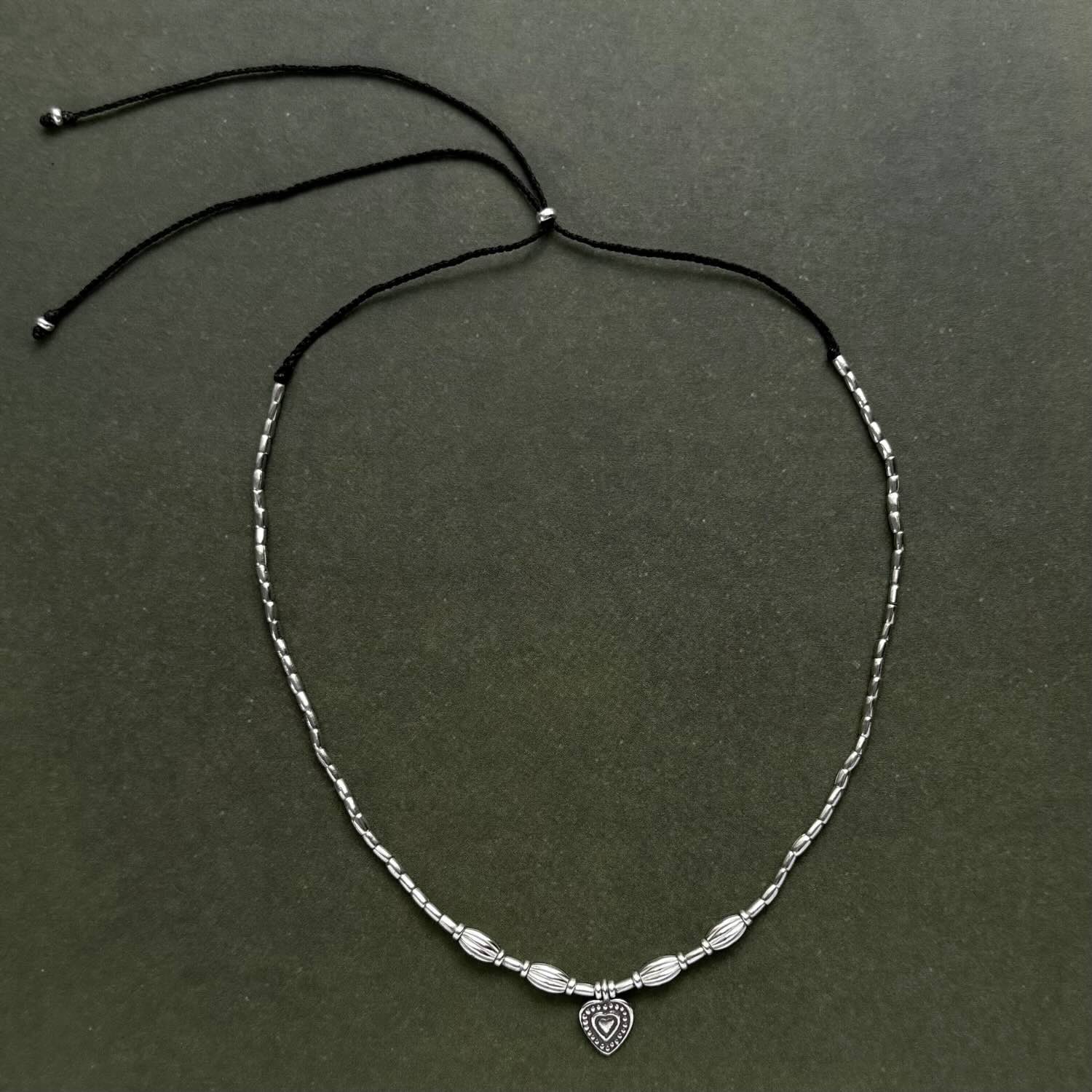Silver beaded necklace with a heart charm on a dark green background