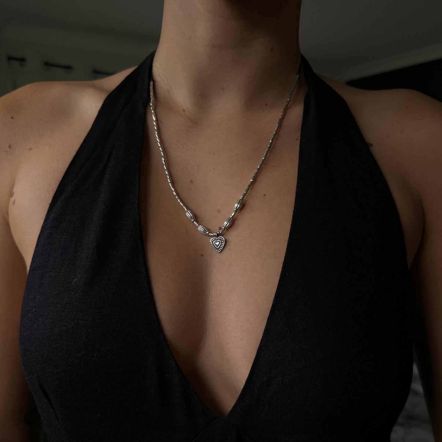Person wearing a black top and silver necklace with a heart pendant.