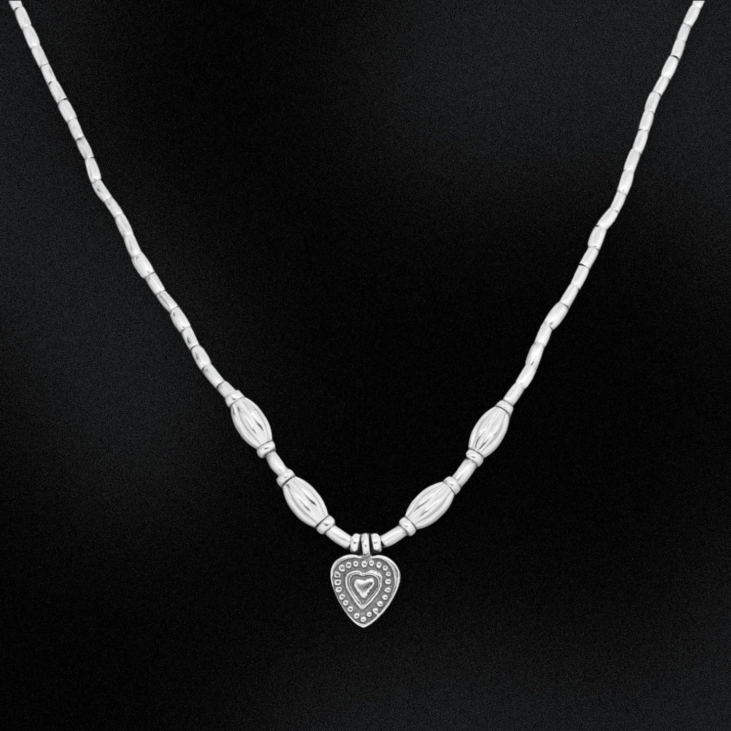 Silver necklace with a heart-shaped pendant on a black background