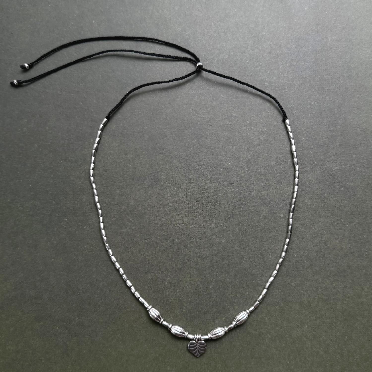 Silver beaded necklace with a heart charm on a gray background