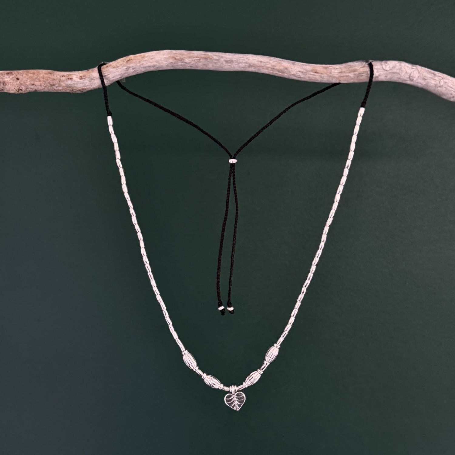 Necklace with leaf pendant on a branch against a dark green background