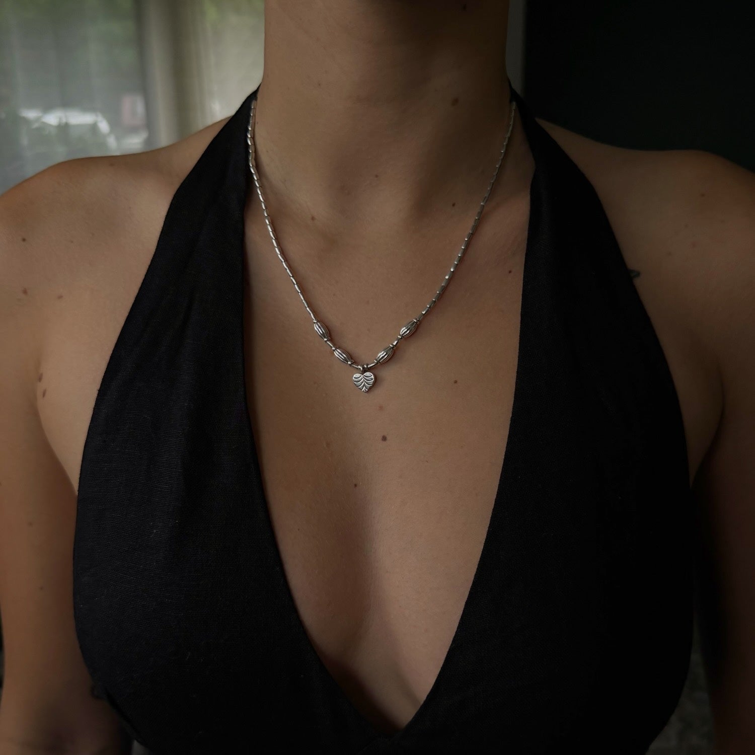 Person wearing a black halter top and silver necklace with heart pendant.