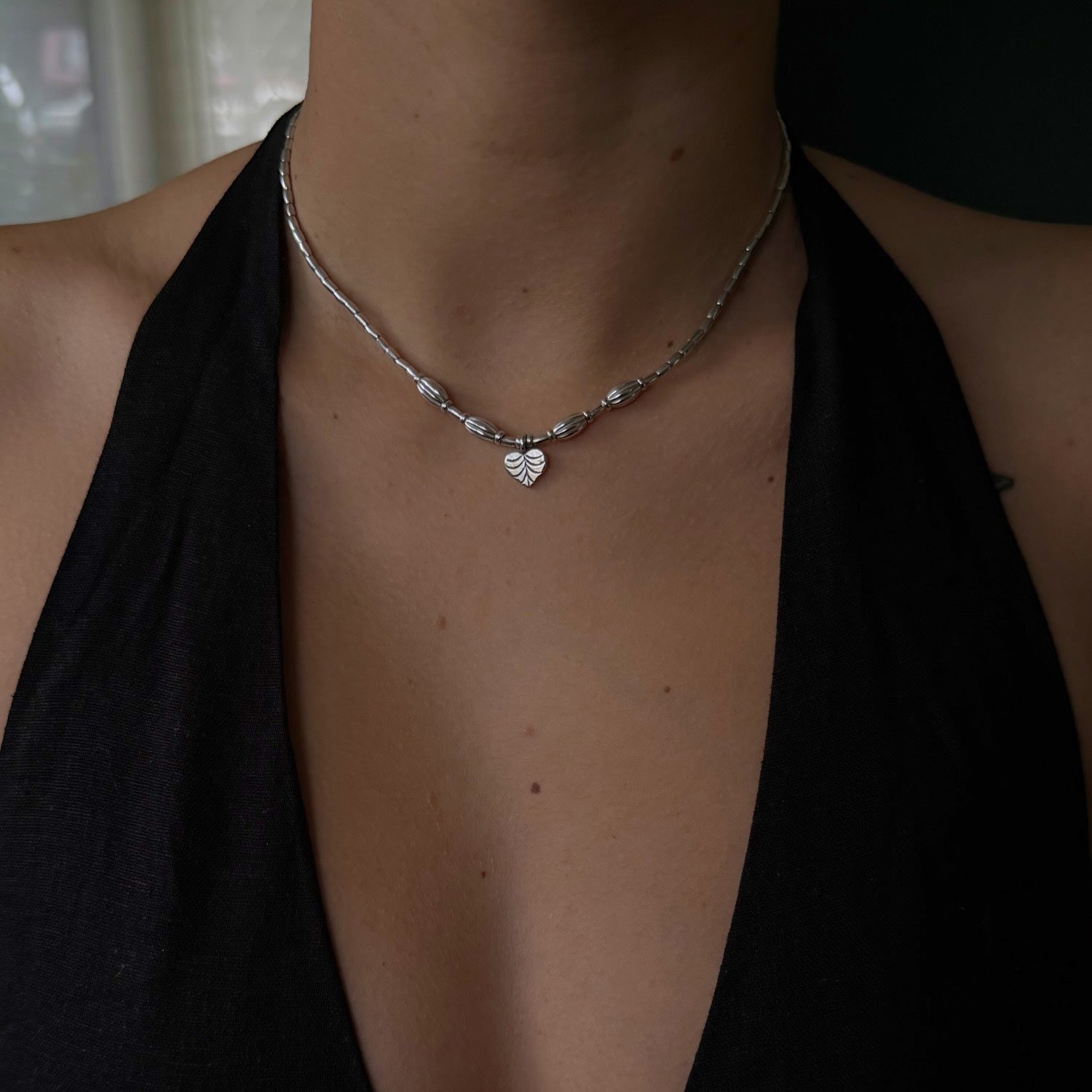 Silver necklace with a heart pendant worn by a person in a black top.