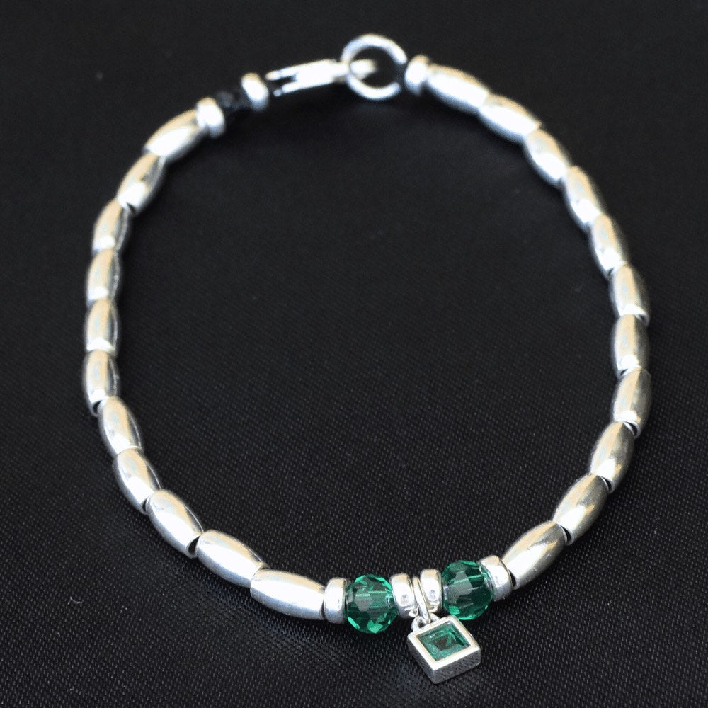 Handcrafted from premium quality sterling silver and embellished with exquisite silver beads, this stunning bracelet boasts a captivating green charm at its centre, surrounded by two alluring green beads on either side. Perfect for those who love a pop of green in their accessories.  To finish the look, the beads are threaded onto a sturdy waxed cord that has been finished with a sleek lobster clasp, making it effortless to wear and comfortable to keep on for hours.