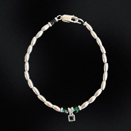 Handcrafted from premium quality sterling silver and embellished with exquisite silver beads, this stunning bracelet boasts a captivating green charm at its centre, surrounded by two alluring green beads on either side. Perfect for those who love a pop of green in their accessories. To finish the look, the beads are threaded onto a sturdy waxed cord that has been finished with a sleek lobster clasp, making it effortless to wear and comfortable to keep on for hours.