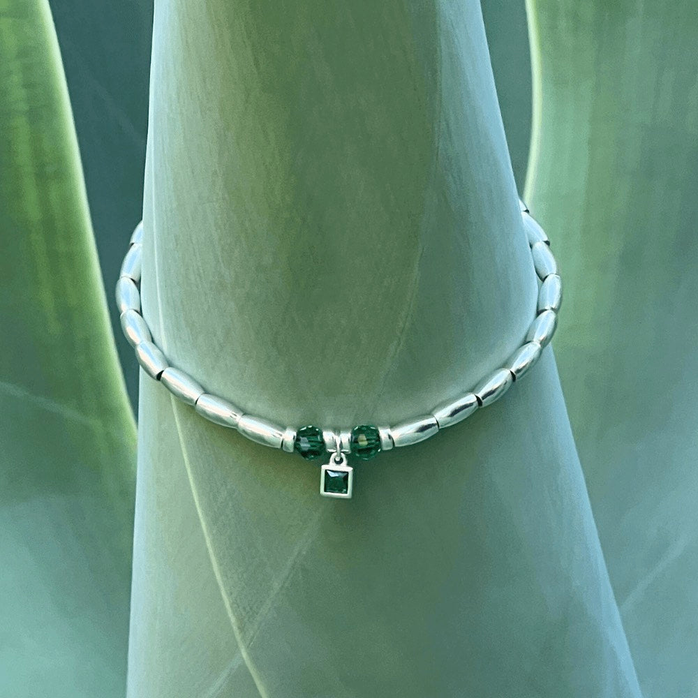 Handcrafted from premium quality sterling silver and embellished with exquisite silver beads, this stunning bracelet boasts a captivating green charm at its centre, surrounded by two alluring green beads on either side. Perfect for those who love a pop of green in their accessories.  To finish the look, the beads are threaded onto a sturdy waxed cord that has been finished with a sleek lobster clasp, making it effortless to wear and comfortable to keep on for hours.