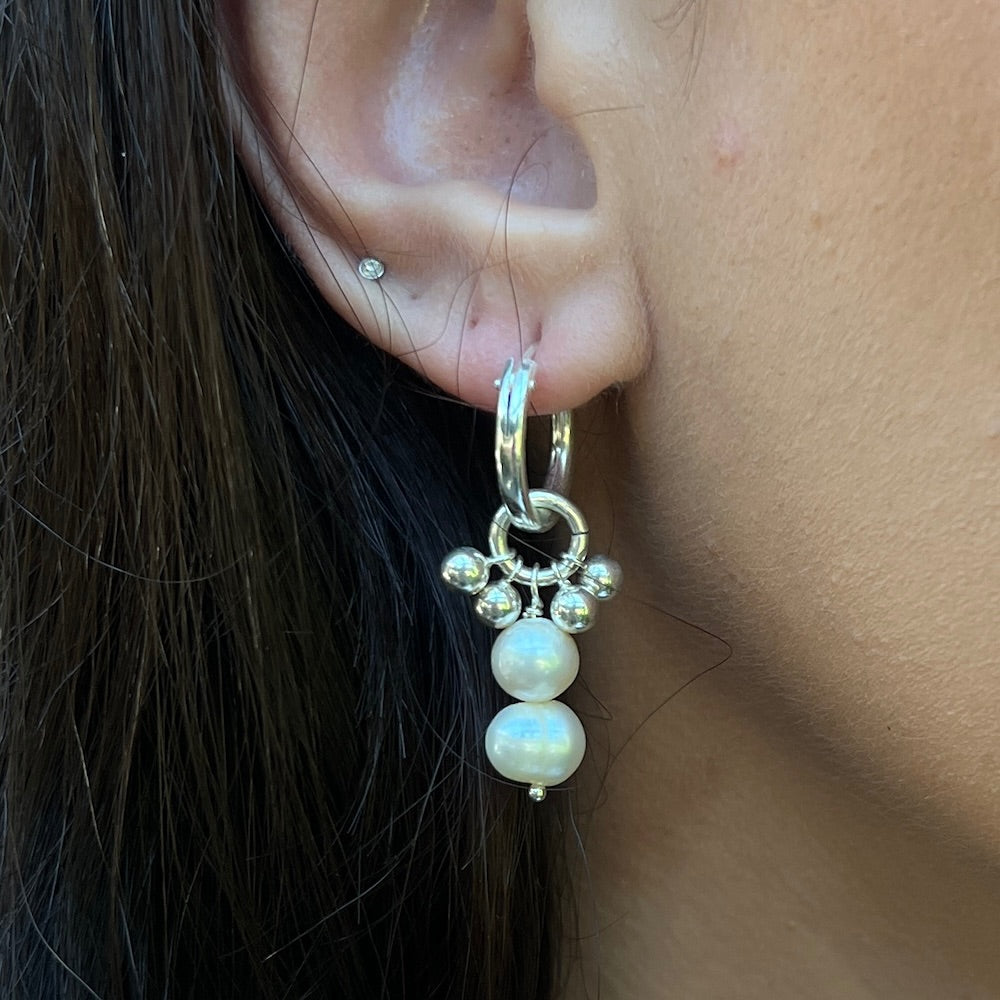 Close-up of an ear wearing a silver earring with pearl-like beads.
