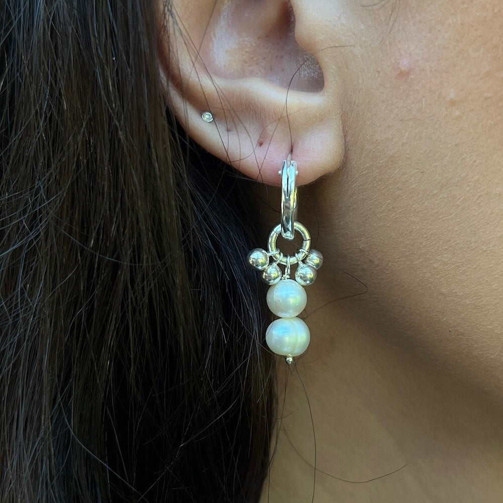 Pearl earring worn on an ear with dark hair and skin background